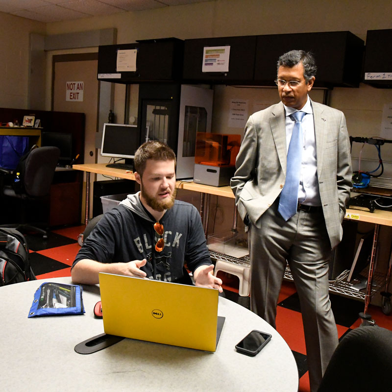 Business person listens to student pitch an idea using a laptop