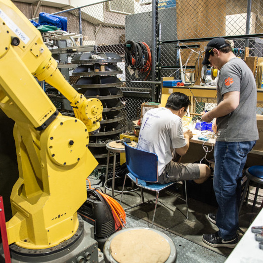 Two students work at a desk behind a large yellow robot