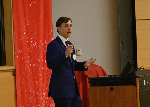 Student in a suit holds microphone and speaks to he audience