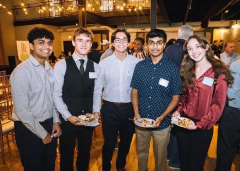 Five students pose at an event each dressed up and wearing a nametag
