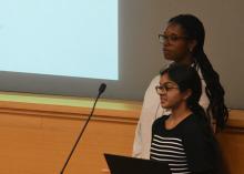 Two students stand in front of a projectd screen and give a presentation
