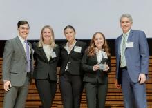 Four students and their advisor pose while holding award