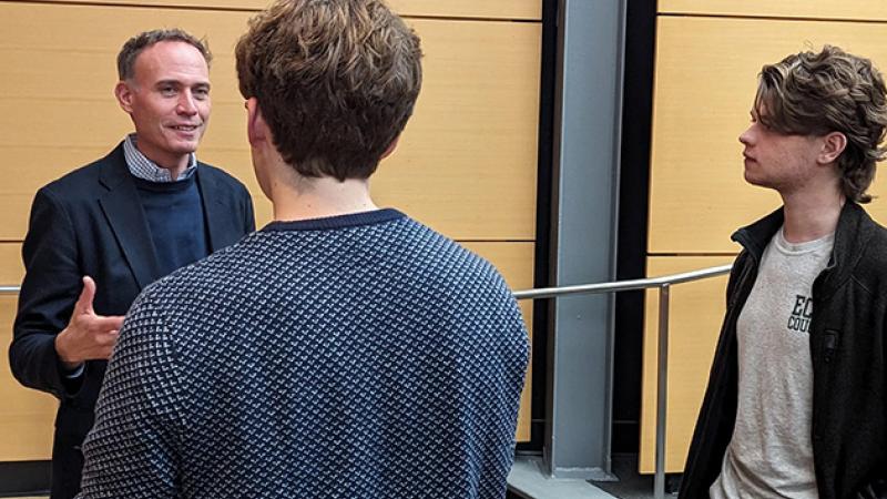 Man talks with two students after a presentation
