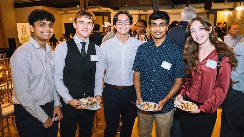 Five students pose at an event each dressed up and wearing a nametag