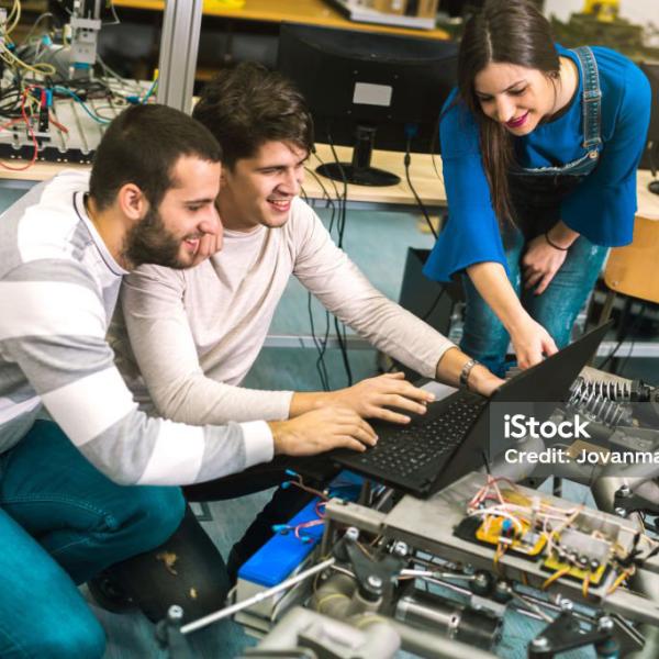 Three students review a laptop in a makerspace environment